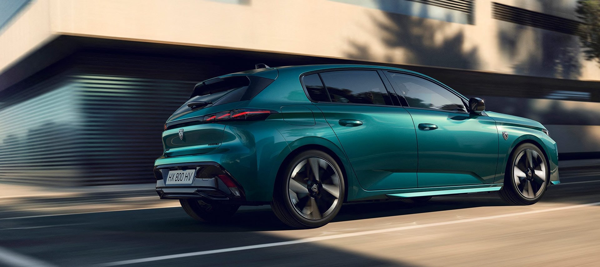 Teal hatchback car driving on a city street.