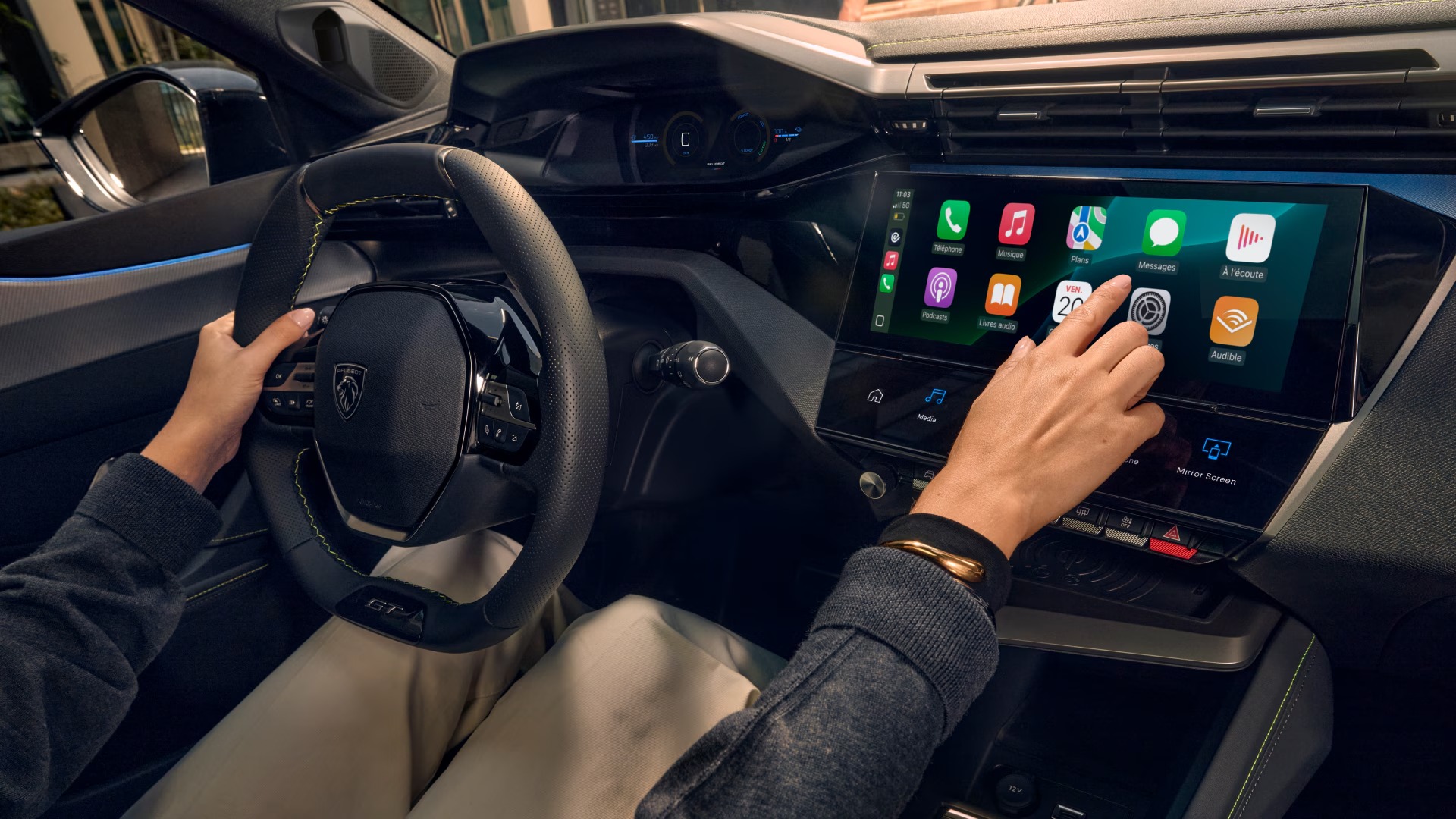 Person using touchscreen in a car next to a steering wheel.