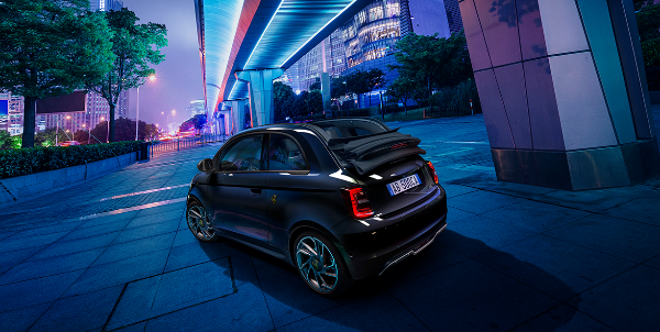 Small car parked under illuminated urban walkway at night.