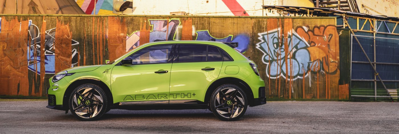 Green Abarth SUV parked beside a graffiti-covered wall.
