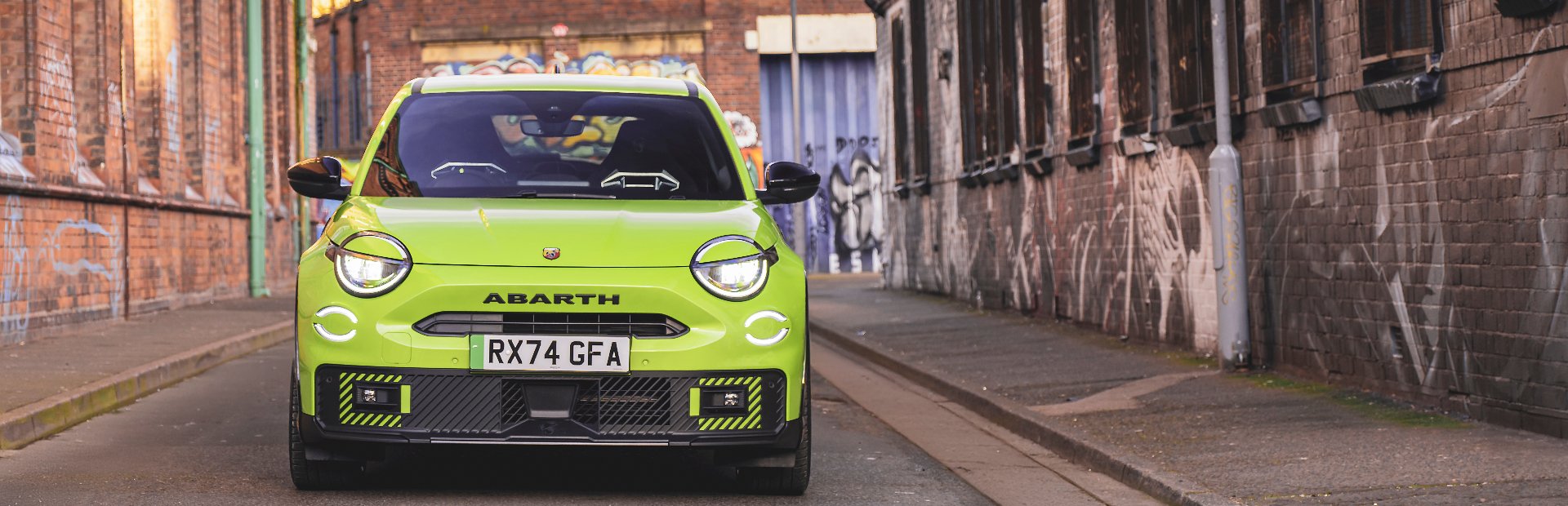 Bright green Abarth car parked in alleyway with graffiti-covered walls.