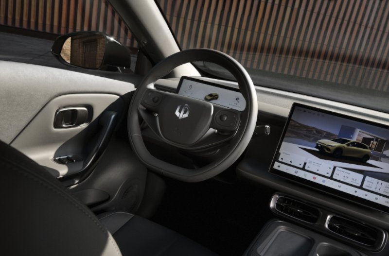 Car interior showing steering wheel, dashboard, and two digital screens with vehicle display.