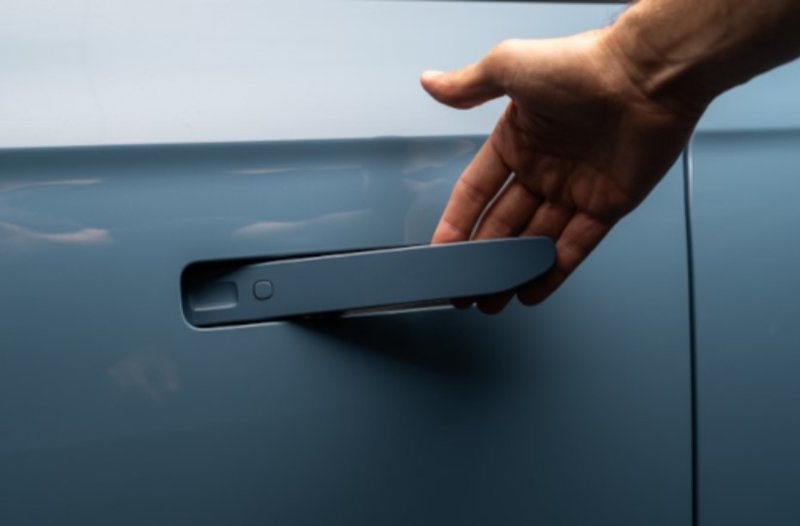 Hand reaching for a blue car's retractable door handle.