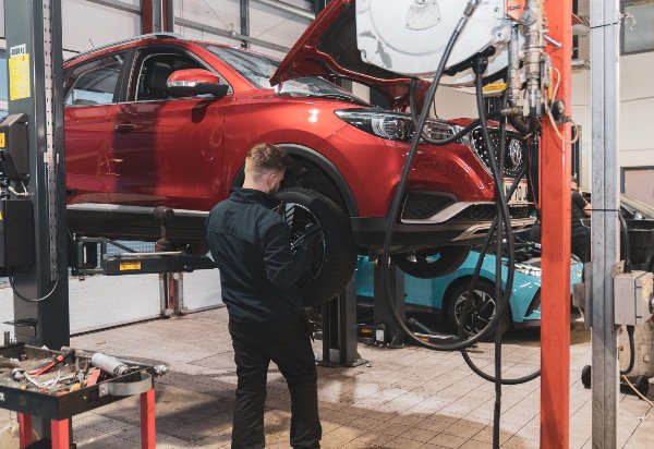Mechanic inspecting a red car on a lift in a garage.