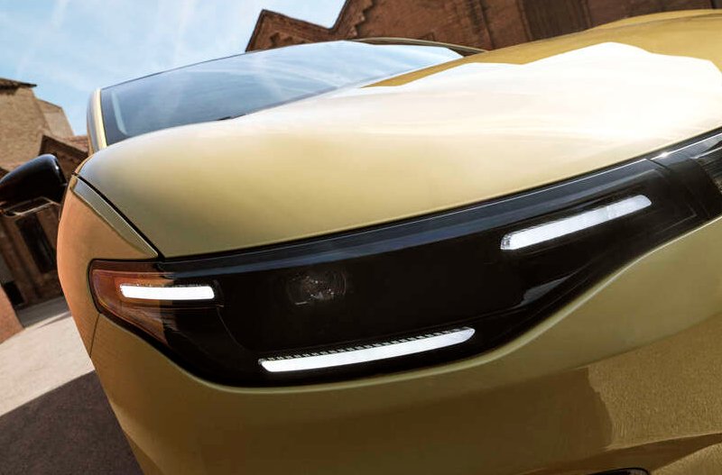 Close-up of a yellow car's front headlight and grille.