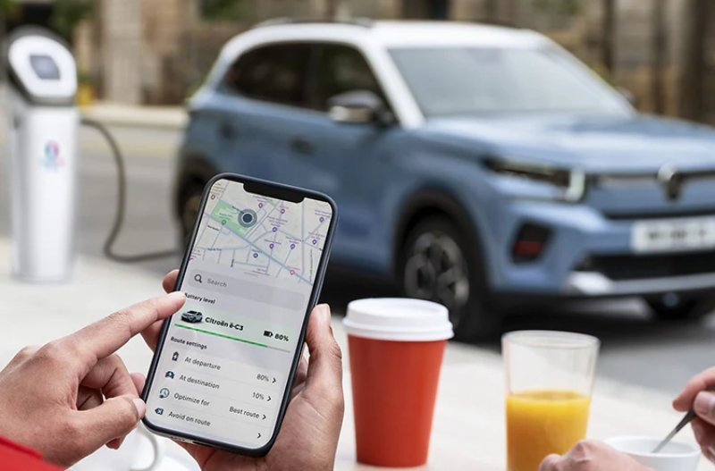 Smartphone displaying a car charging app, with a parked blue electric car in the background.