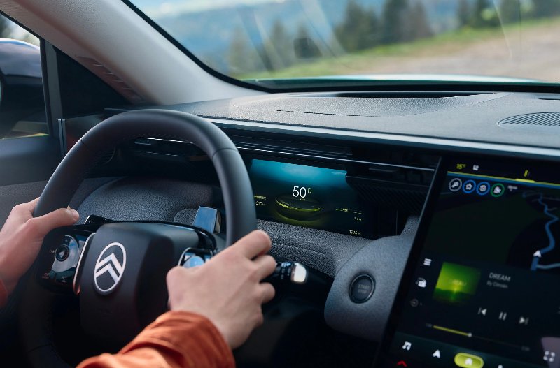 Close-up of hands on a Citroën car steering wheel, view of dashboard displays and navigation.