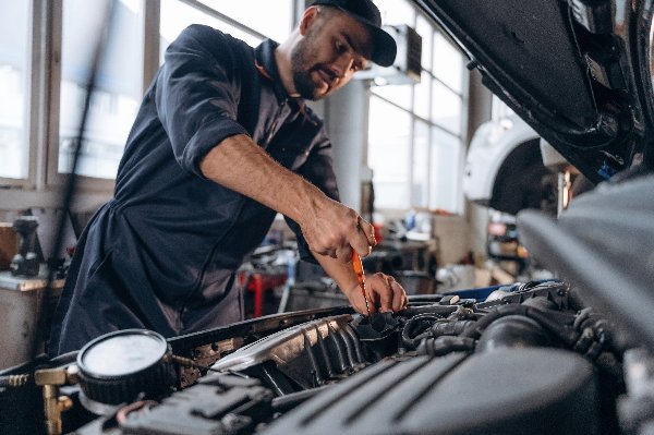 Mechanic working on a car engine with a screwdriver in a workshop.