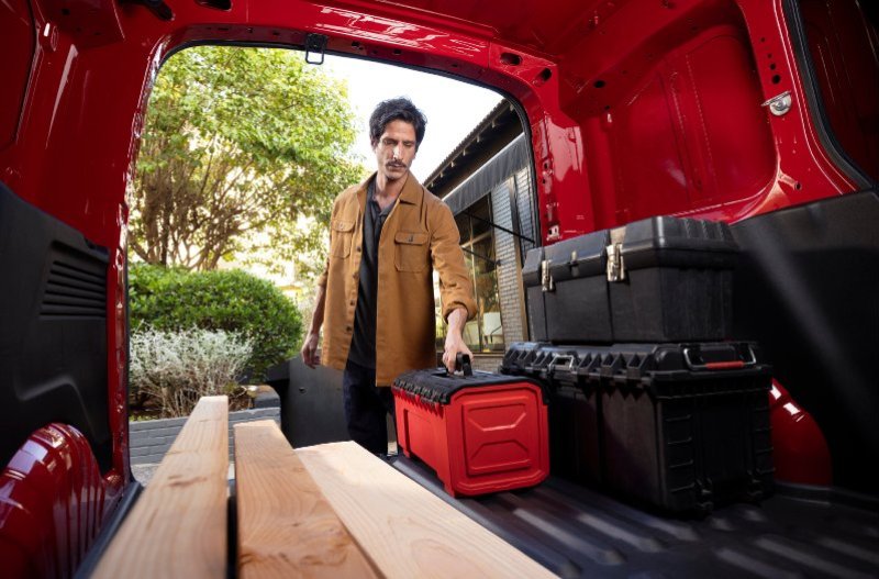 Man loading toolboxes into a red van with wooden planks inside.