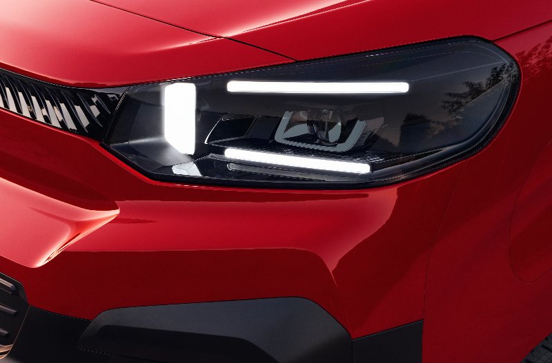 Close-up of a red car's front left LED headlight and grille detail.