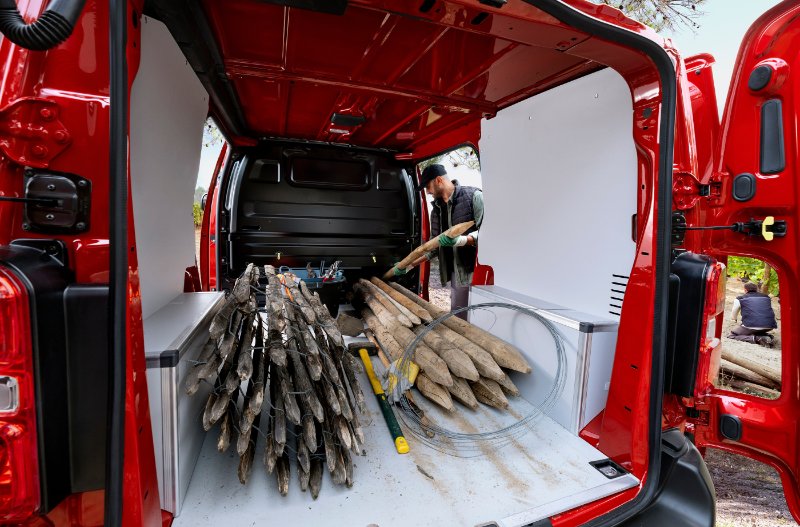 Open van with tools, wooden stakes, and a man loading materials inside.