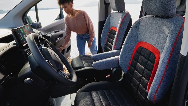 Car interior with steering wheel, display screen, grey and black seats, person entering vehicle.