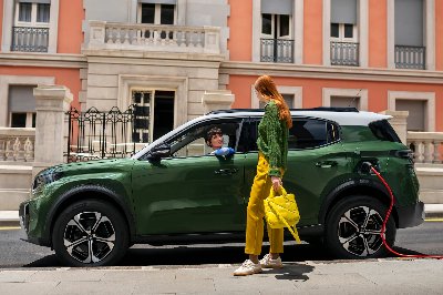 Green electric car charging with two people interacting beside it.