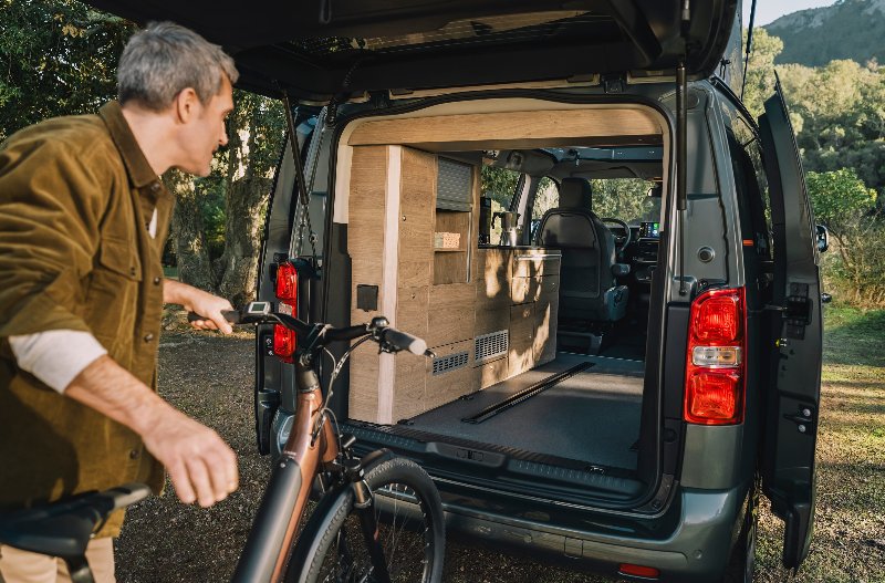 Man placing bicycle into the back of an open van with fitted interior cabinets.