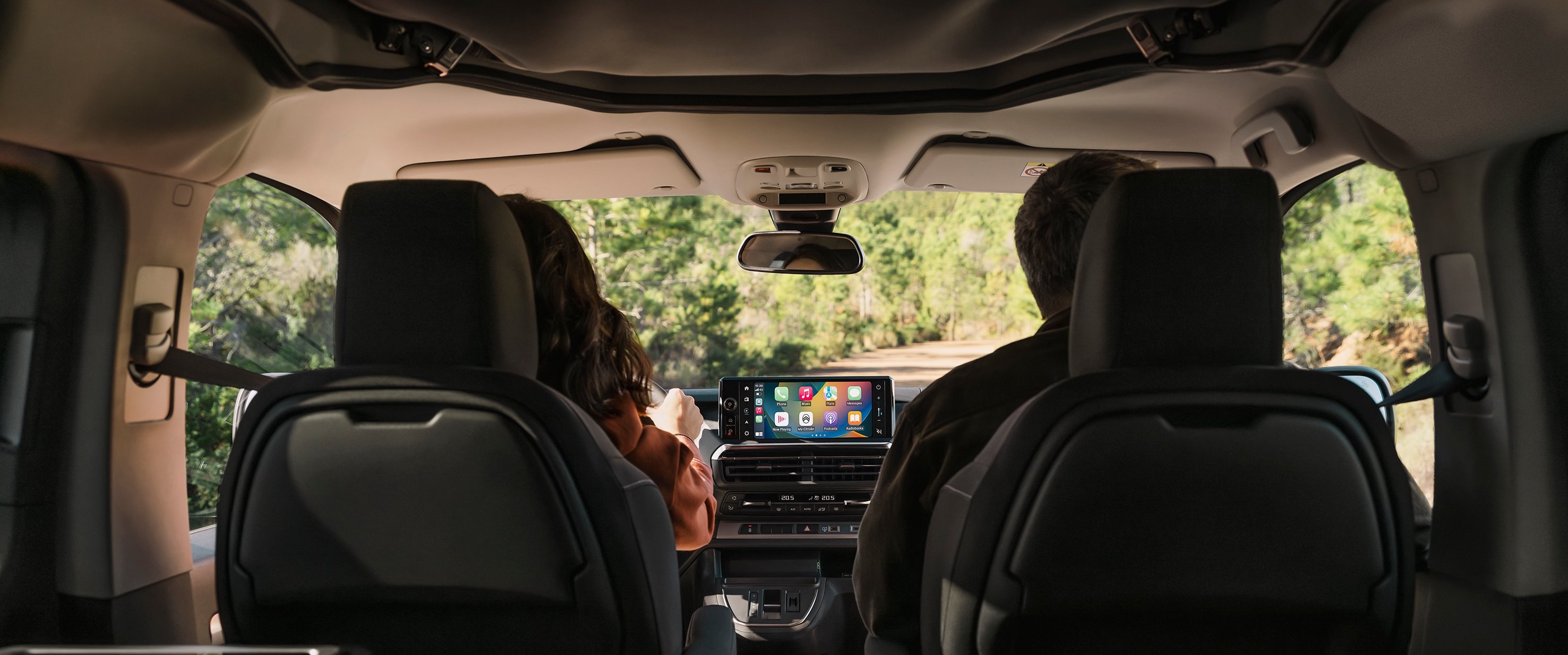 Interior view of a car with two people in the front seats and a central display screen.
