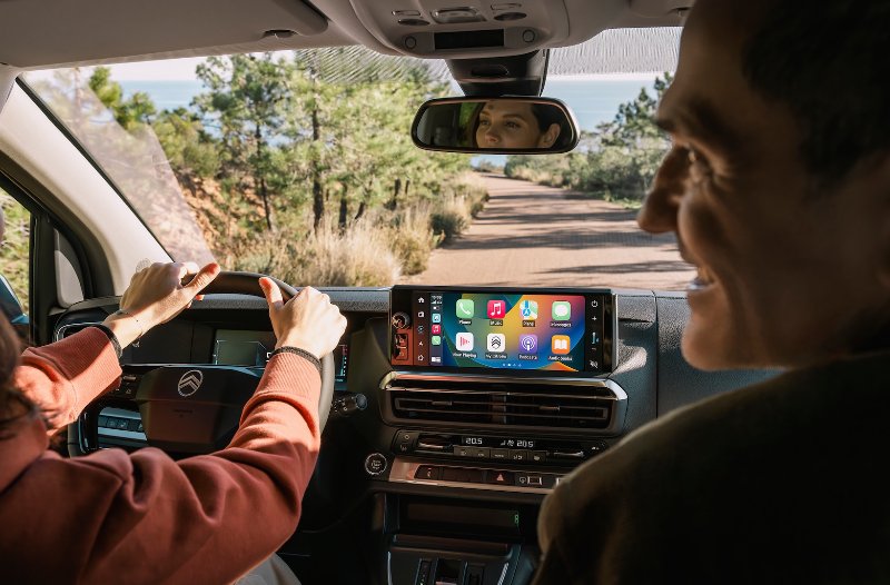 Two people in a car interior with dashboard screen displaying apps while driving.
