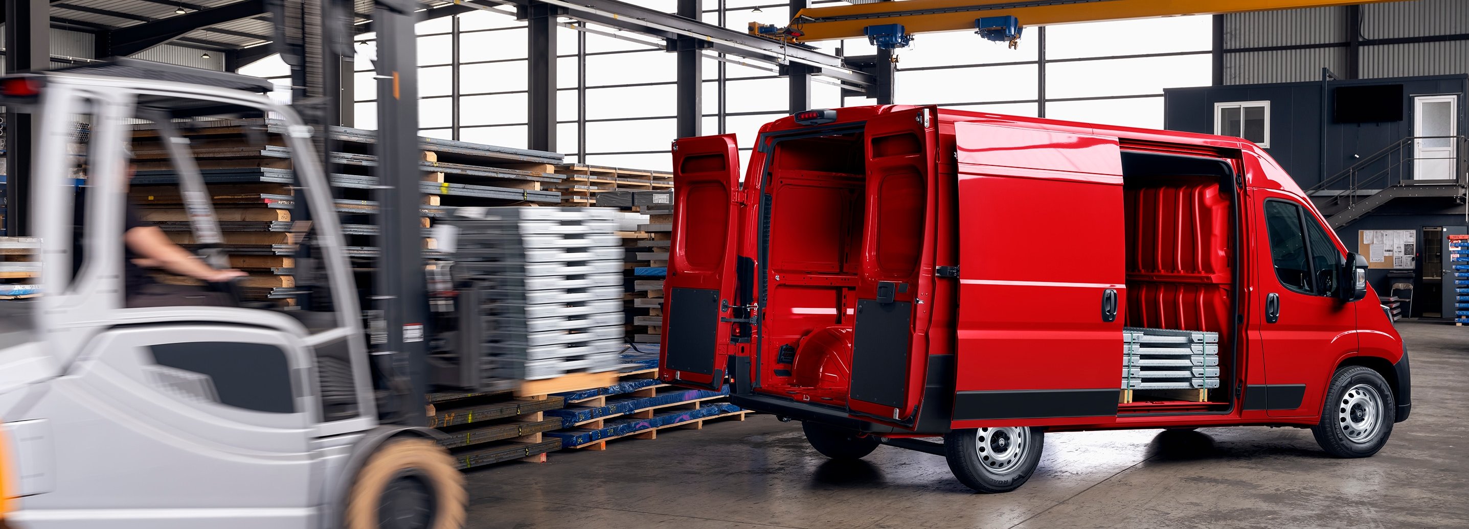 Red van with open doors next to a forklift in an industrial warehouse.