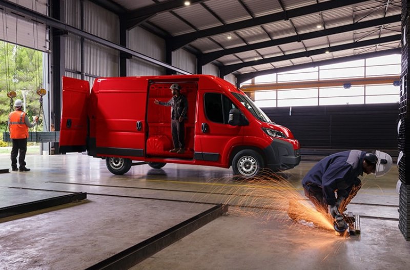 Red van in a warehouse, with workers using tools nearby.