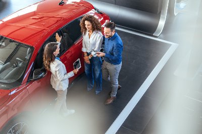 People discussing beside a red car in a showroom.