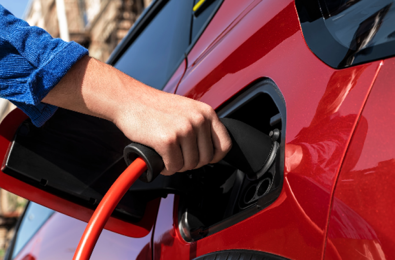 Hand plugging a charging cable into a red electric car.