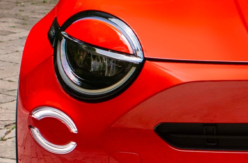 Close-up of a red car's headlight and part of the front grille.