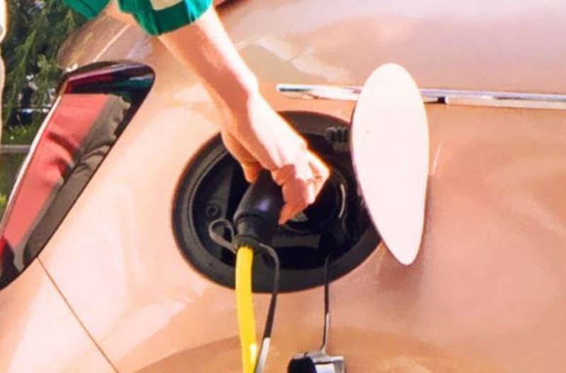Hand plugging a charging cable into an electric car.