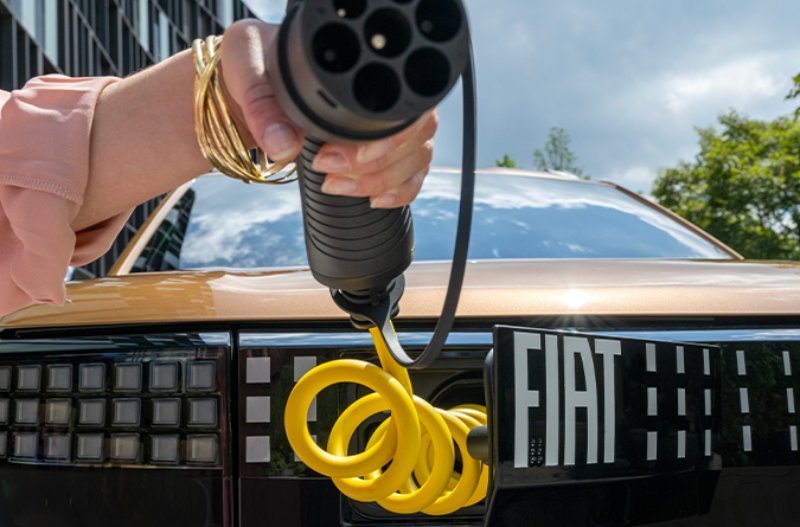 A person holding an electric vehicle charging cable near a Fiat car.