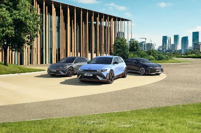 Three modern cars parked on a circular driveway near a building with vertical wooden beams.