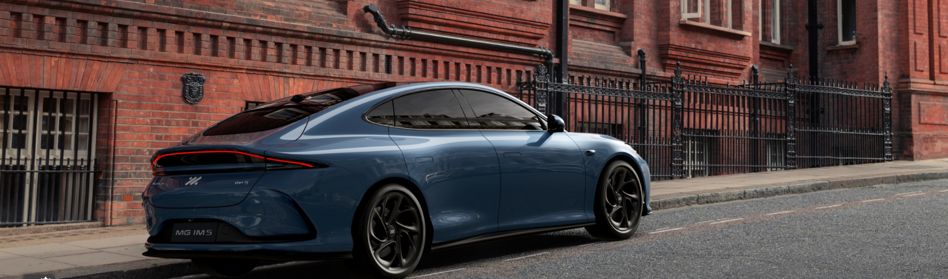 Blue MG IM5 car parked beside a red brick building.