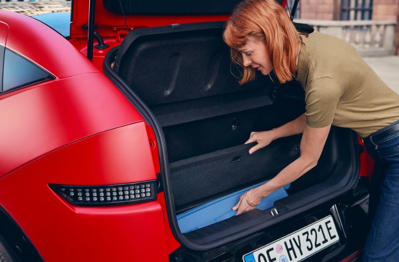 Woman placing an item into the boot of a red car.