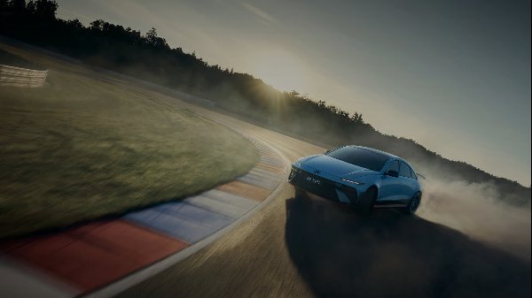 A blue car drifting around a race track corner with sunlight in the background.
