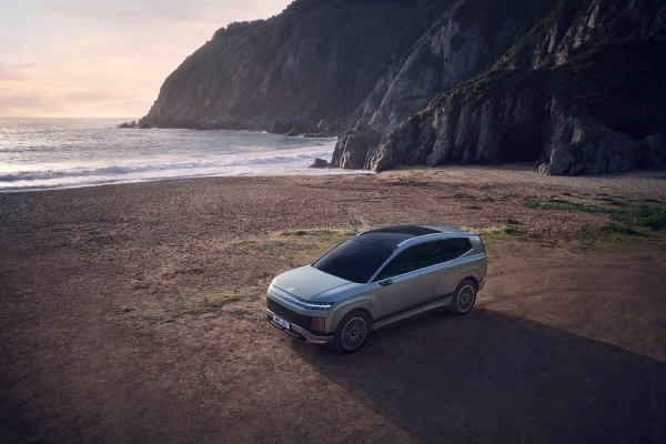 Silver SUV parked on a sandy beach near rocky cliffs and the sea.