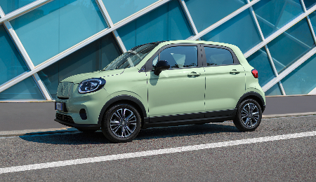 A light green compact car parked on a street beside a modern glass building.