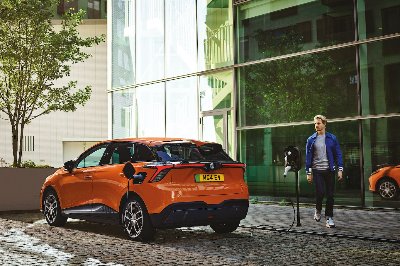 Orange electric car charging, with a person walking towards it.