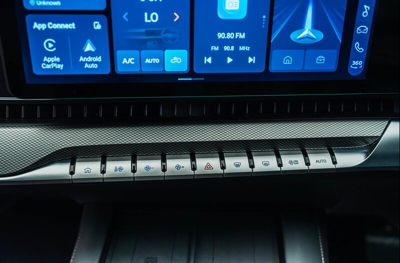 Car dashboard with touchscreen display and physical control buttons below it.