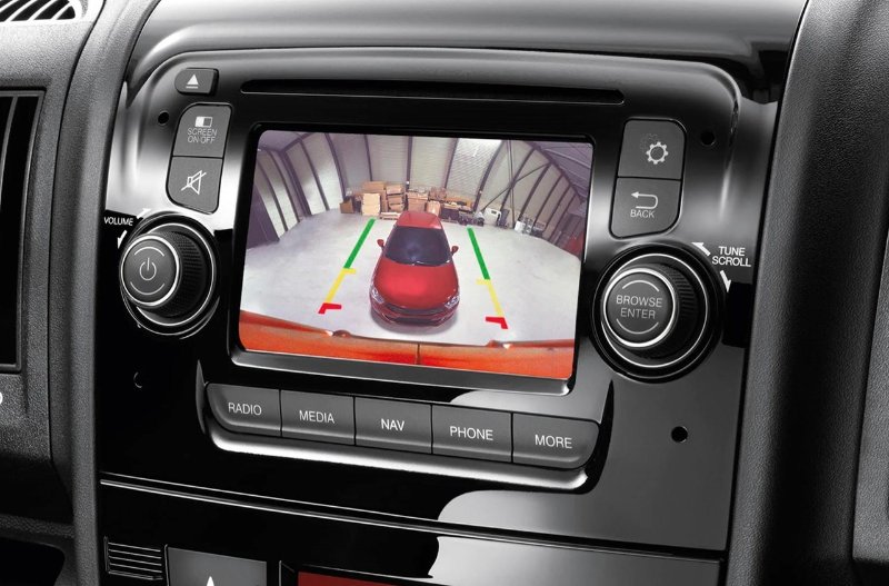 Car dashboard with rearview camera showing a red vehicle and parking guidelines.