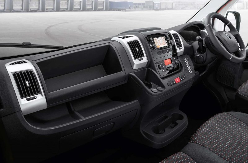 Van interior with steering wheel, dashboard, control panel, and patterned seats.