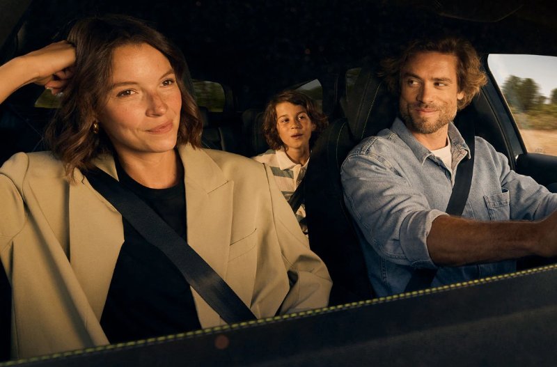 A family of three smiling while driving in a car.