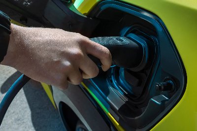 Hand plugging charging cable into a green electric vehicle.