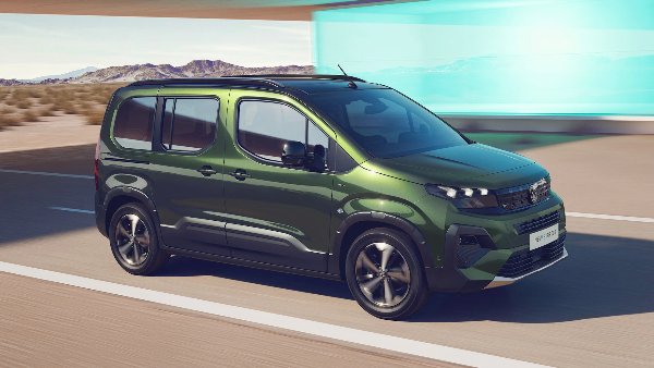 Green van driving on a road with mountains in the background.