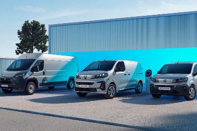 Three electric vans parked side by side, each connected to a charging station.
