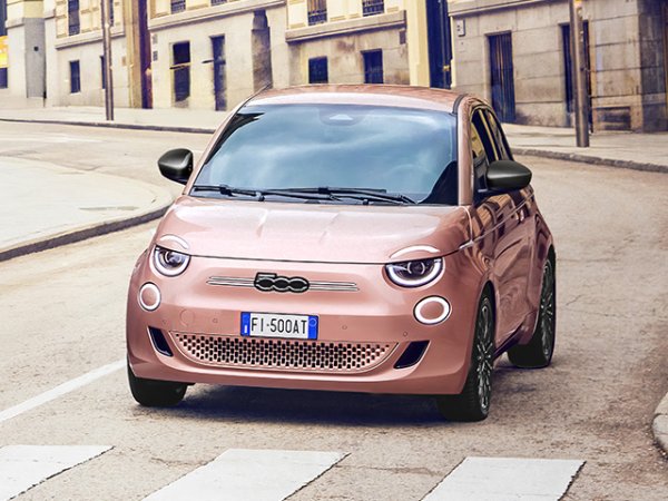 Pink Fiat 500 car parked on a cobblestone street.