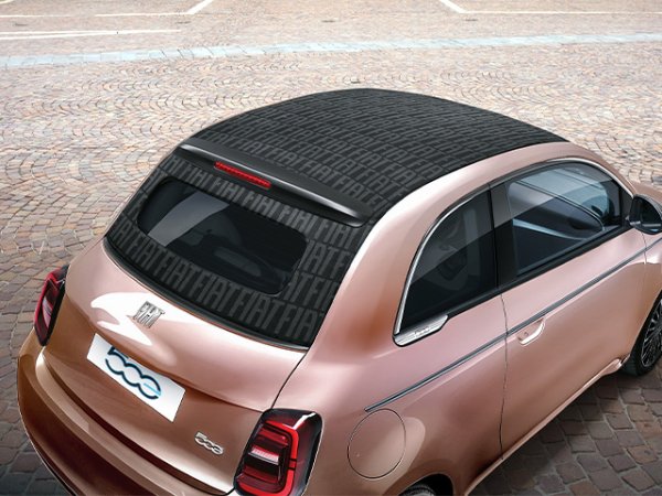 A bronze Fiat 500 with a patterned black roof parked on cobblestone pavement.