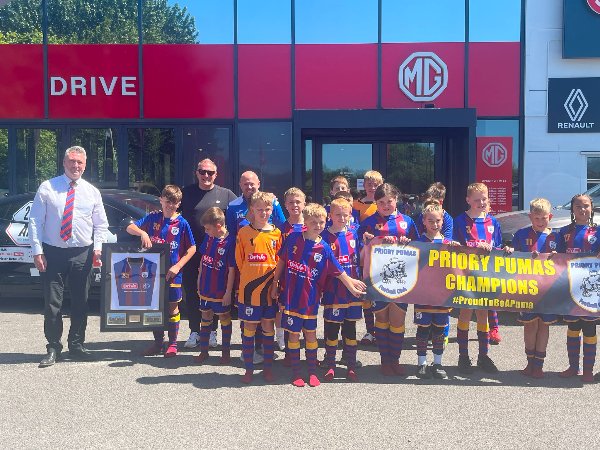 Football team holding a Priory Pumas Champions banner at an MG and Renault dealership.