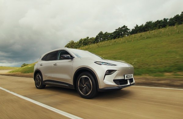 Silver electric SUV driving on a road with a grassy hillside.