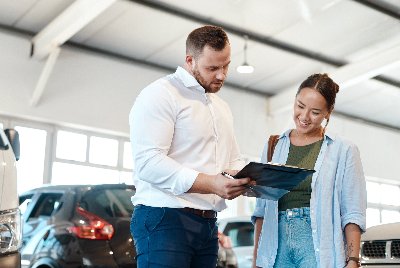Man showing a document to a woman in a car showroom.