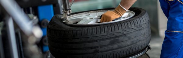 Mechanic in blue overalls removing a tyre from a wheel using machinery.
