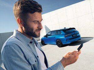 Man using a smartphone beside a parked blue hatchback.