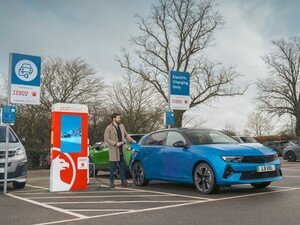 Man charging a blue electric car at a public charging station.